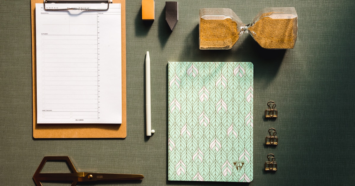 Clipboard, notebook, pen, hourglass, and stationery arranged on a dark surface