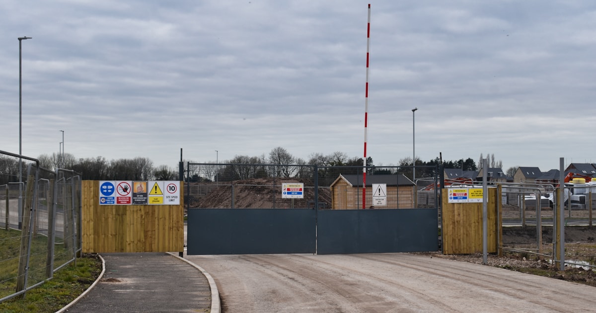 Closed construction-site entrance with a barrier gate and warning notices